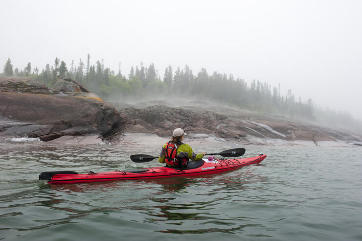 Woman paddling a red sea kayak in the fog.