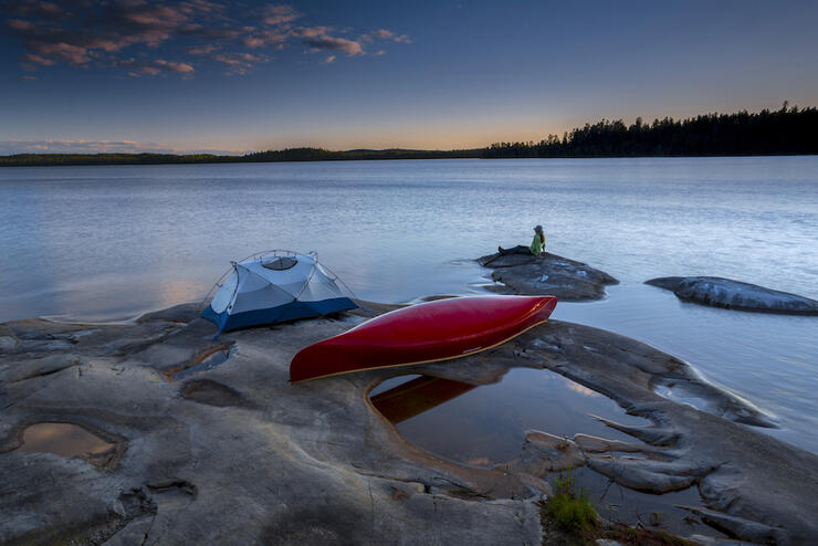 Tent and canoe on smooth rock by lakes edge at sunset camping on crown land in Ontario.