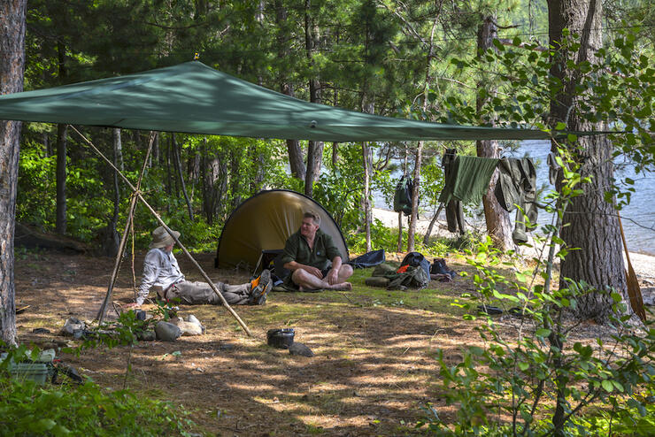 Two men sitting on a forest campsite on crown land in Ontario. 