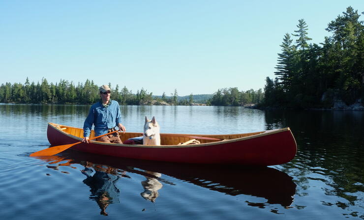 Man paddling a red canoe with a dog sitting in it. 