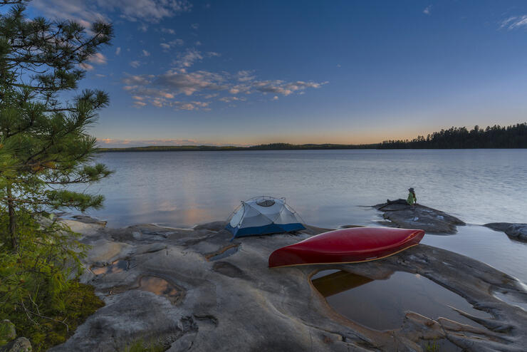 Tent and canoe on smooth rocky point at sunset.