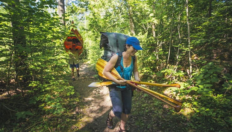 Woman carrying paddles and pack and man carrying a canoe on a portage