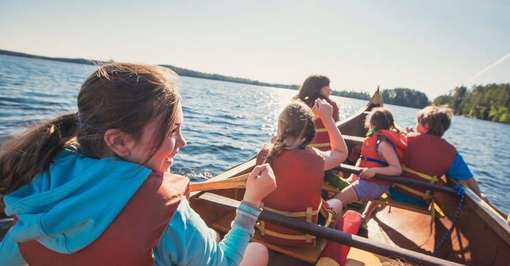 Children smiling while paddling in a voyageur canoe. 