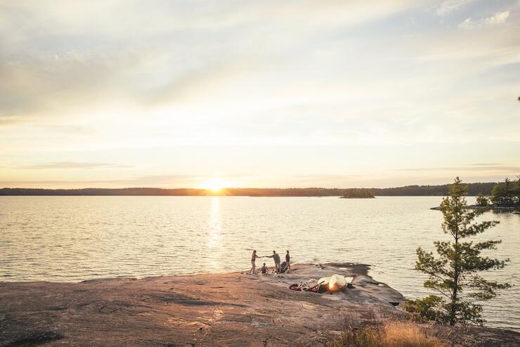 Family with canoes pulled up on shore at the edge of a lake.