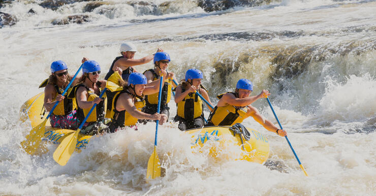 Seven people with paddles in a yellow raft in whitewater 