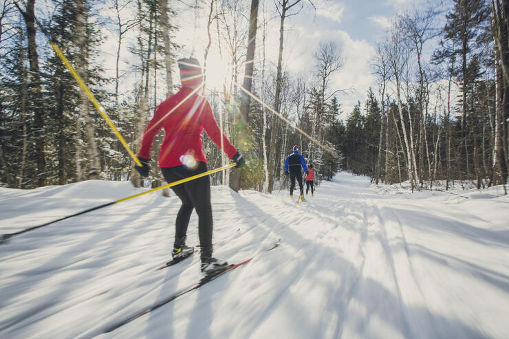 Three people cross country skiing on groomed trail 