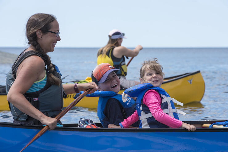 Two kids sitting in front of stern paddler in canoe.