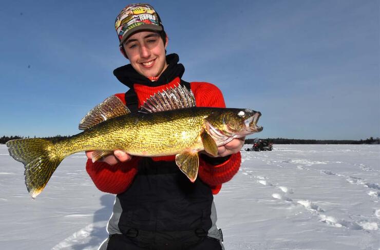 young male ice angler holding walleye