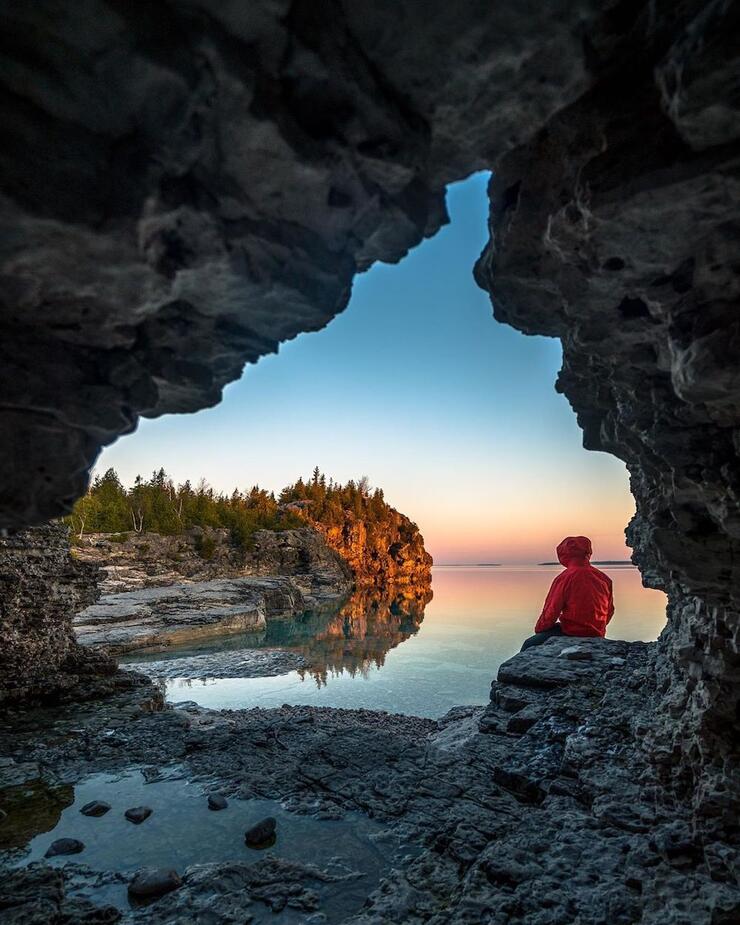 Person sitting in cave next to a lake