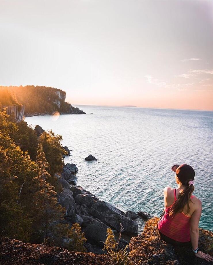 Woman sitting on cliff overlooking the water.