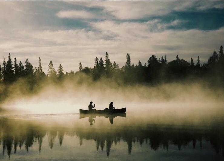 Two people paddling canoe on a misty morning on the lake
