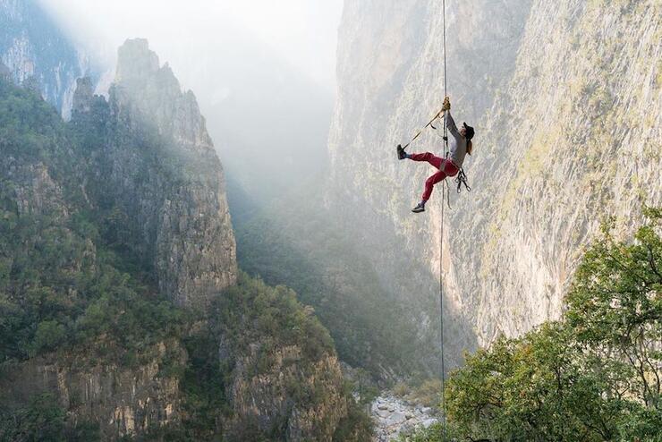 Person hanging onto a rope beside a mountain