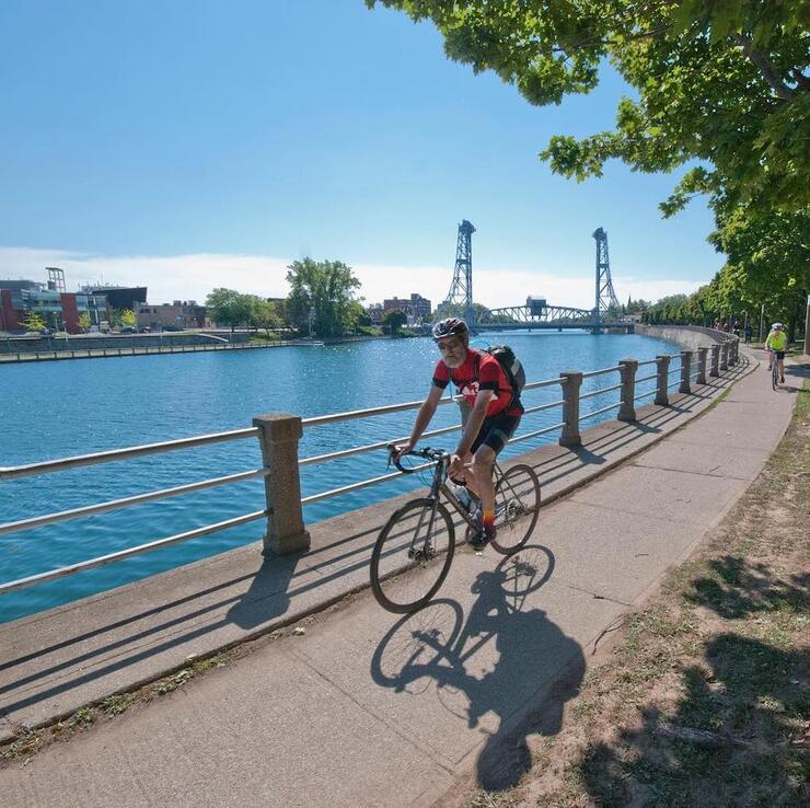 Man riding bike next to waterway on paved trail
