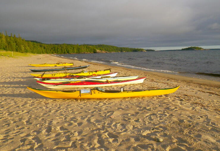 7 sea kayaks lined up on sand beach 