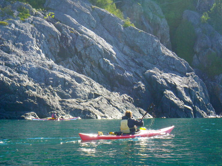 Sea kayaking paddling in turquoise waters near rock cliffs