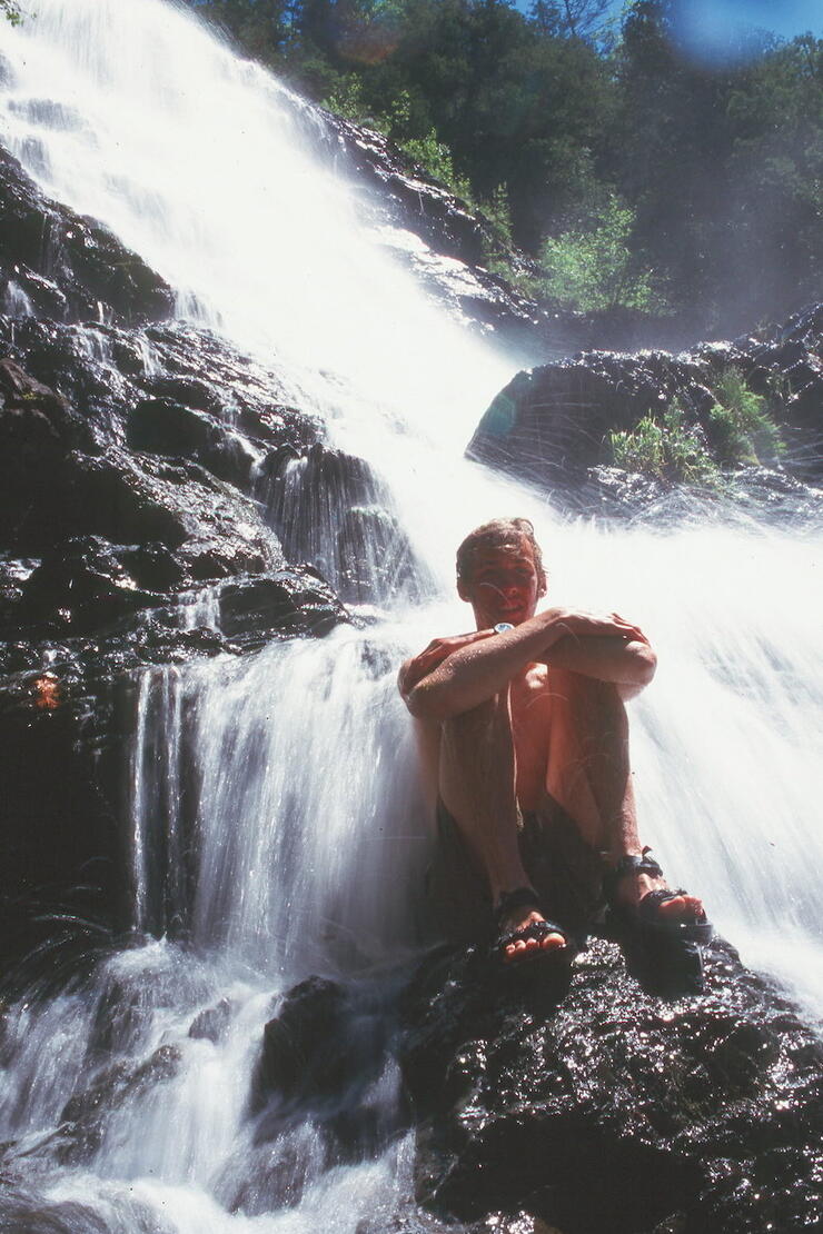Man sitting on rock at bottom of waterfalls 
