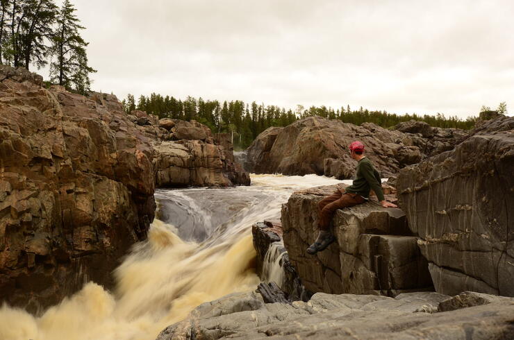 Man sitting on rocks beside rushing waterfall 