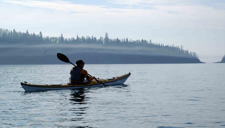 A person in a sea kayaking paddling in misty waters