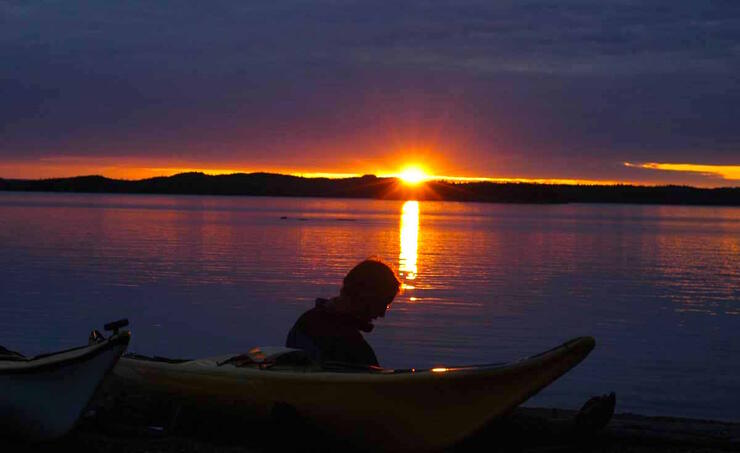 Man watching sunset while sitting on beach beside kayaks
