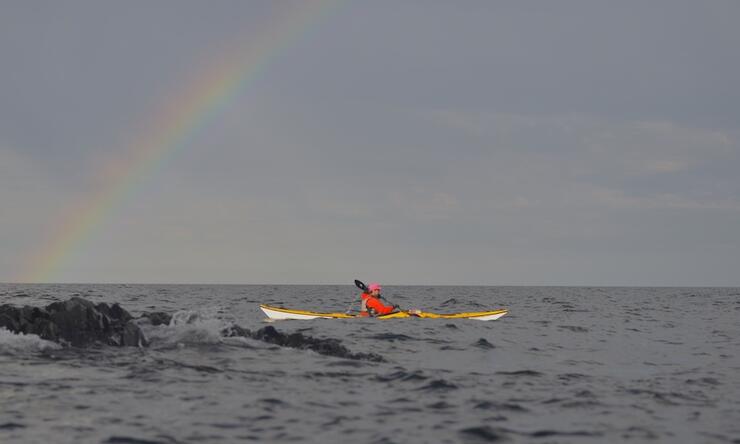 Person sea kayaking with rainbow in sky