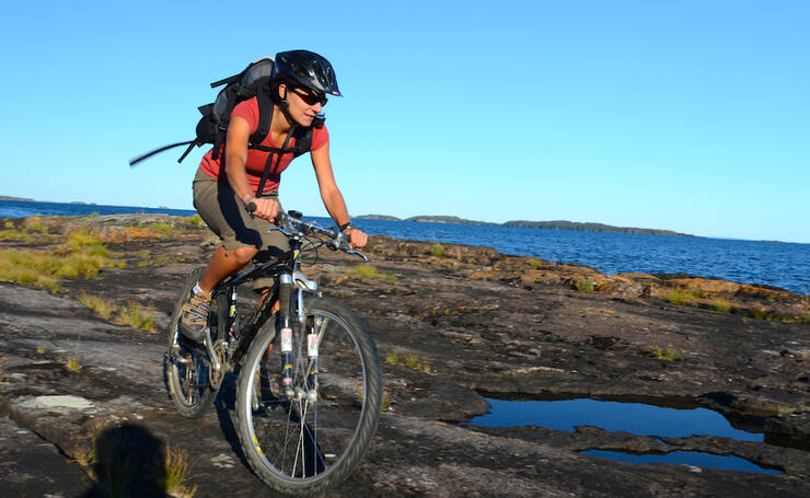 Woman riding a mountain bike over flat rocky surface with a lake in background.