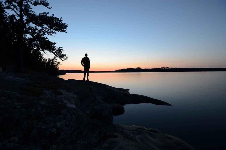 Sillouette of a man standing on rocky shoreline of lake at sunset