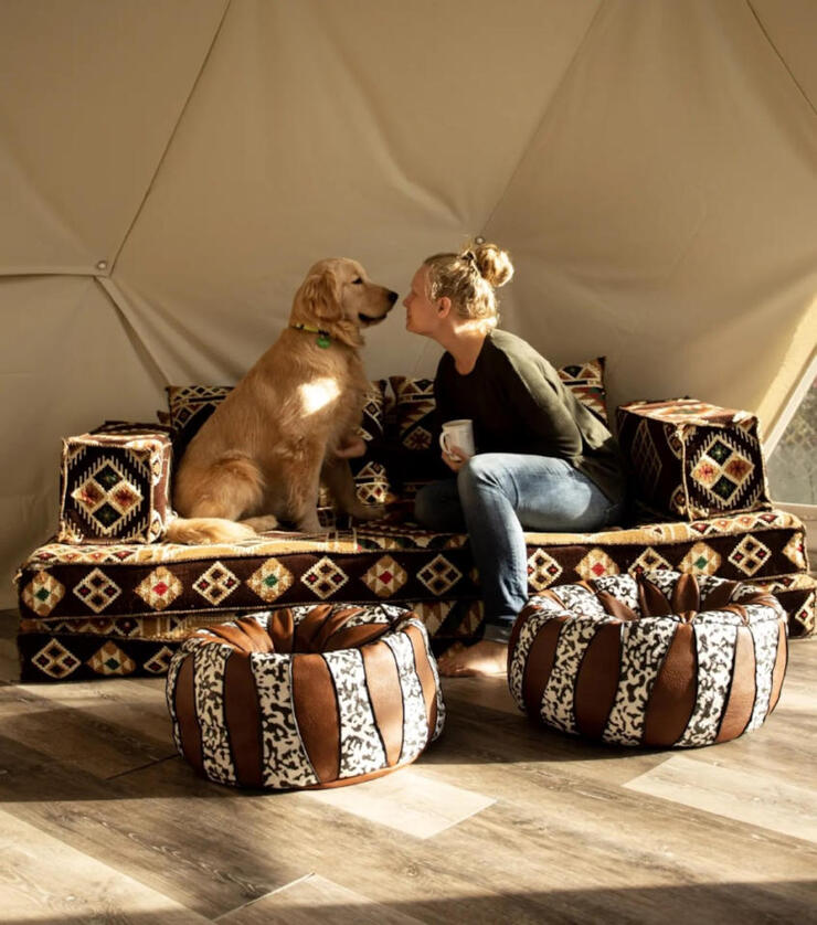 woman and dog sit nose to nose on comfy couch in a camping dome