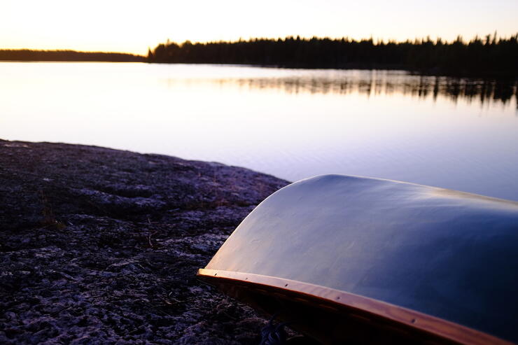 Canoe resting on gunnels on shoreline of lake at sunset