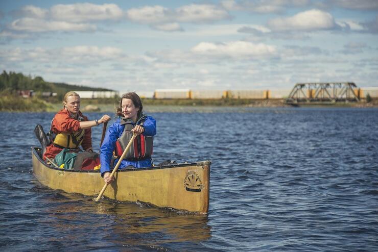 Two people paddling canoe with bridge in background